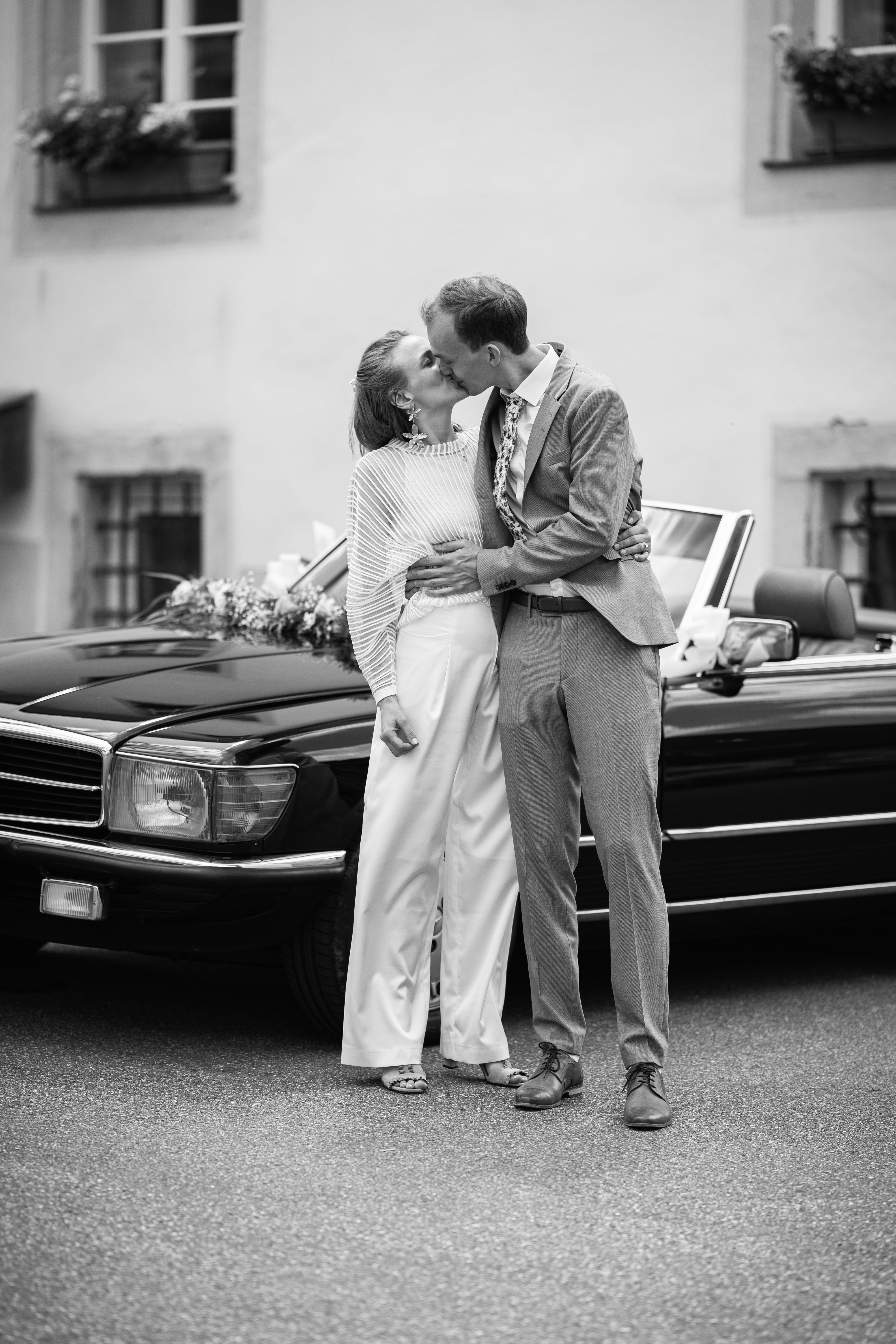 küssendes Brautpaar vor Oldtimer